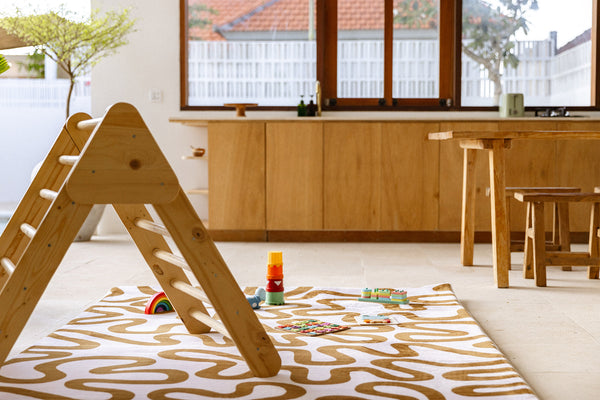 Indoor play area with wooden climbing frame and toys on a patterned playmat