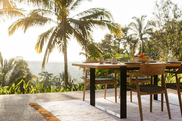 Outdoor dining set on a white rug with tropical backdrop